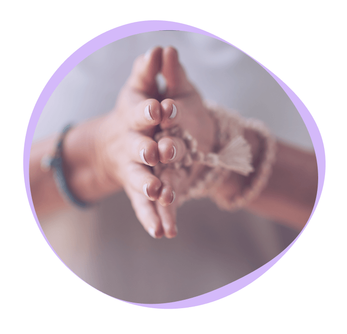 Close-up of hands in a prayer or meditation gesture, wearing beaded bracelets, with a soft purple border around the image.